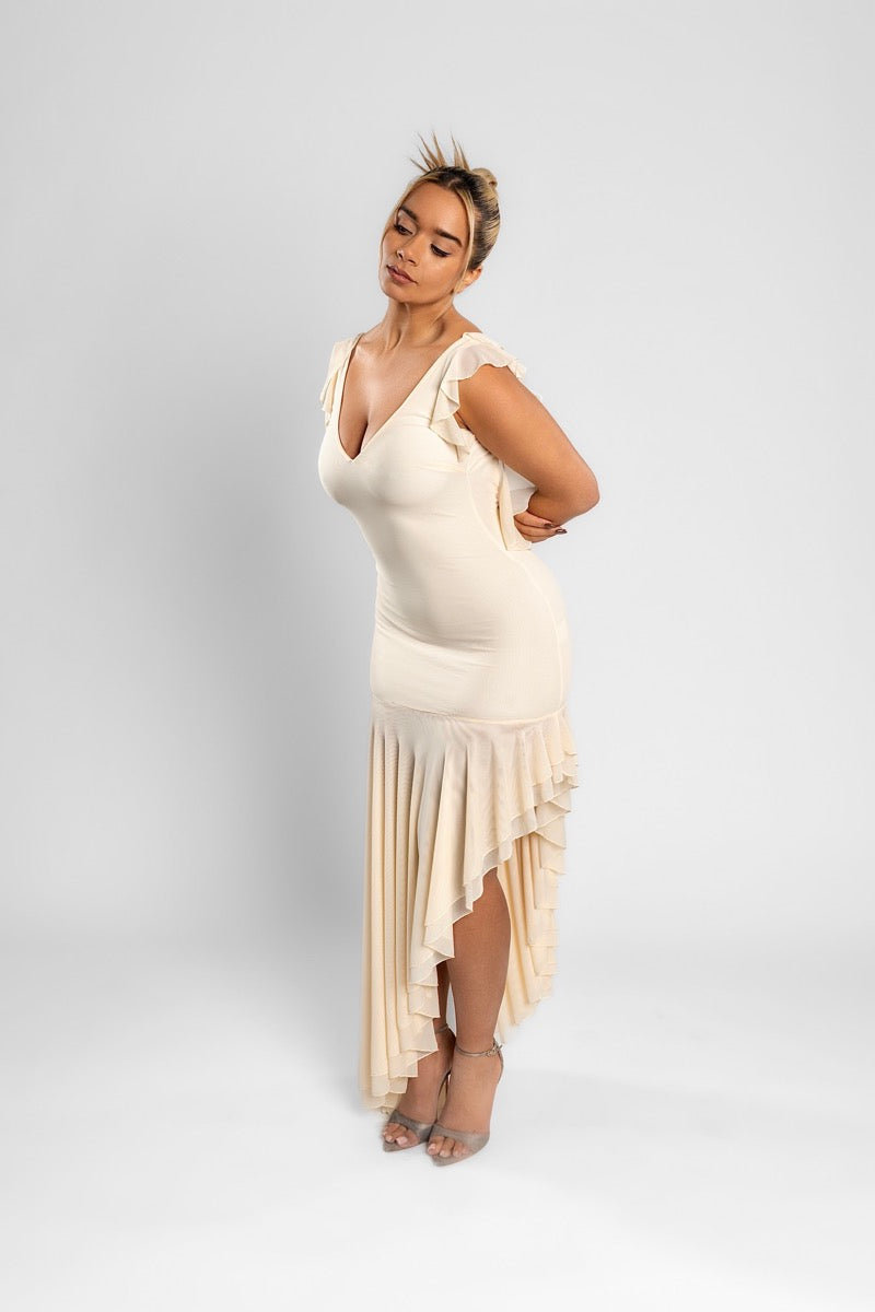 Woman in the cream AMARAÉ Juniper dress with a V neckline, ruffled cap sleeves and an asymmetric ruffle hem, against a plain light grey studio backdrop