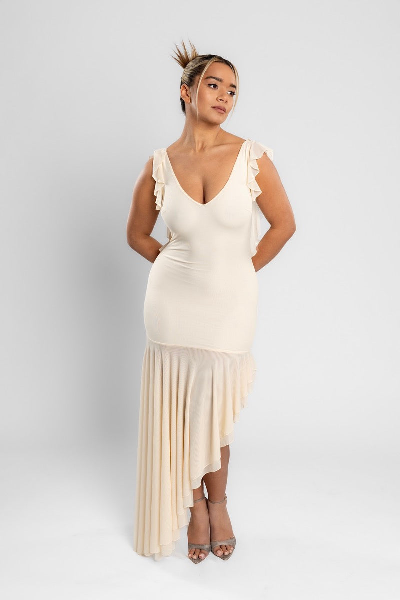 Woman in the cream AMARAÉ Juniper dress with a V neckline, ruffled straps and an asymmetric mesh ruffle hem, standing against a plain light grey studio backdrop